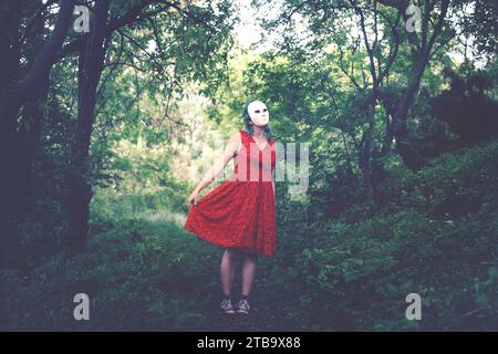 woman with mask on her face and red dress dancing in a forest, abstract concept Stock Photo