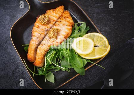 Grilled Butterfly salmon steak with cherry tomatoes and arugula salad on a black square plate. Black plate for serving the dish. Stock Photo