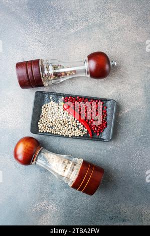 Pepper mills with different types of peppers and sea salt. Spices in glass grinding mills. Top view. Stock Photo