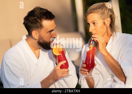 couple in white bathrobes drinking cocktails and looking at each other at a hotel Stock Photo