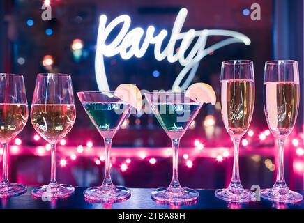 Assortment of alcoholic drinks Martini, wine, champagne glasses on bar with colorful lights background, party celebration concept Stock Photo