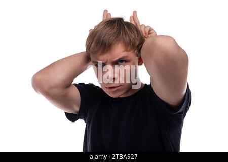 Cute teenage guy with blond hair dressed in a black T-shirt makes a face Stock Photo