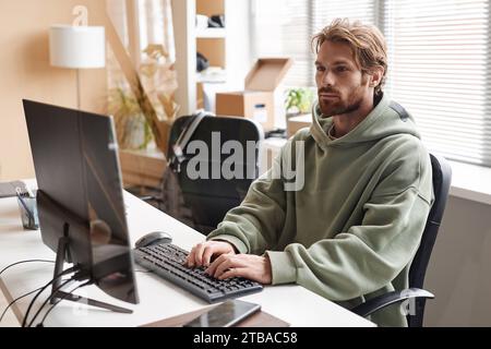 Portrait of young bearded software developer using computer and typing on keyboard while working in office, copy space Stock Photo