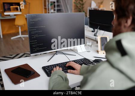 Over shoulder view at software developer writing code in office with focus on computer screen, copy space Stock Photo