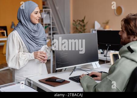 Portrait of Muslim young woman talking to male colleague and smiling while working in IT development, copy space Stock Photo