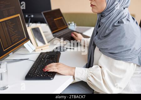 Closeup of Muslim young woman working as female software developer and writing code with multiple computer devices, copy space Stock Photo