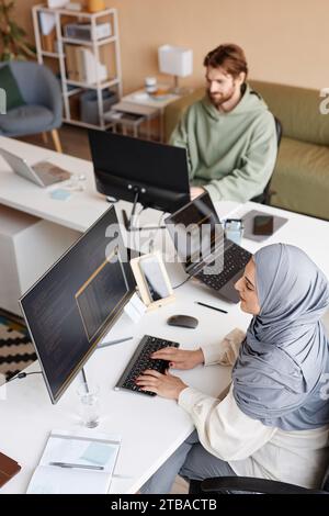 High angle portrait of two people working in IT developers office with Muslim young woman as female programmer writing code Stock Photo