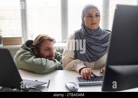 Front view at two people in IT development team working on computer together with Muslim young woman typing Stock Photo