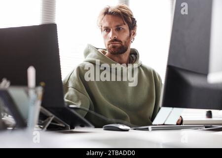 Front view portrait of bearded software developer working on IT project using multiple computer devices Stock Photo