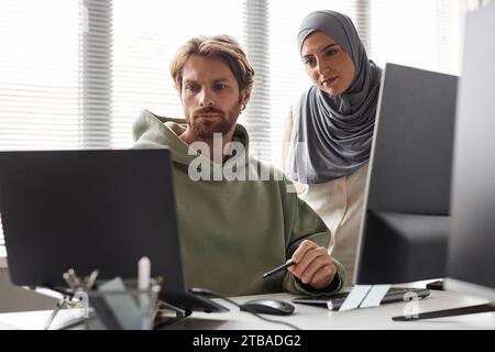 Portrait of IT team with Muslim young woman reviewing project and looking at computer screen Stock Photo