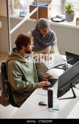 Vertical portrait of IT team of two people reviewing project together in office and using computers Stock Photo
