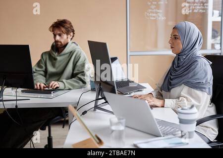 Side view portrait of young Middle Eastern woman working with multiple computers in IT development studio, copy space Stock Photo
