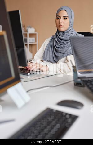 Vertical portrait of young Middle Eastern woman using computer and writing code in IT development office Stock Photo