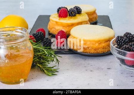 Mini cheesecakes, orange marmalade, rosemary, lemon, and fresh berries close-up on the kitchen table. Cheesecake recipe Stock Photo