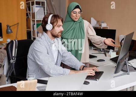 Side view portrait of team of two young IT developers discussing project ideas in office and pointing at computer screen Stock Photo