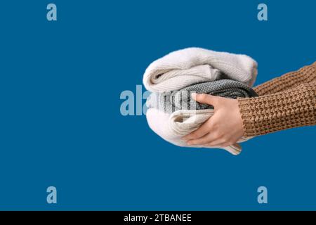 Female hands with stack of different stylish sweaters on blue background Stock Photo