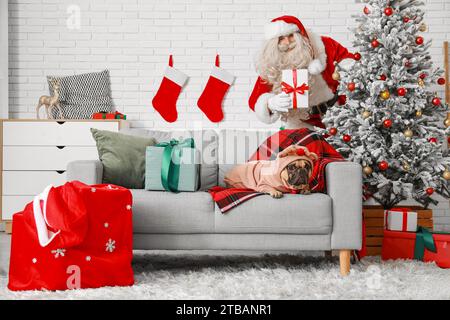 Cute French bulldog wearing pet clothes and Santa Claus with Christmas gifts at home Stock Photo