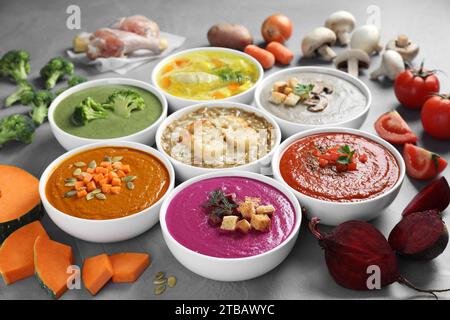 Tasty broth, different cream soups in bowls and ingredients on table, closeup Stock Photo