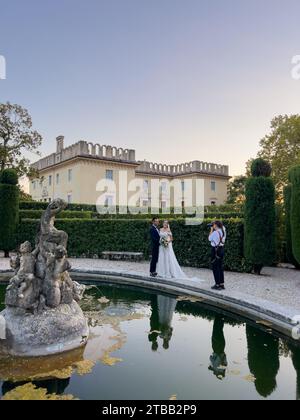 Rome, Italy - 09 august 2023: Girl-photographer photographs bride and groom near the fountain in the garden of an old villa Stock Photo