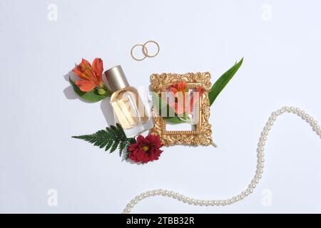 Advertising scene for perfume product with minimal concept. A glass spray bottle decorated with red flowers, green leaves and pearl necklace on a whit Stock Photo