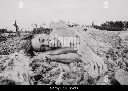 funny adult farmer taking sleep a nap on sheep wool mulch ready for planting cabbage in organic vegetable garden during summertime Stock Photo