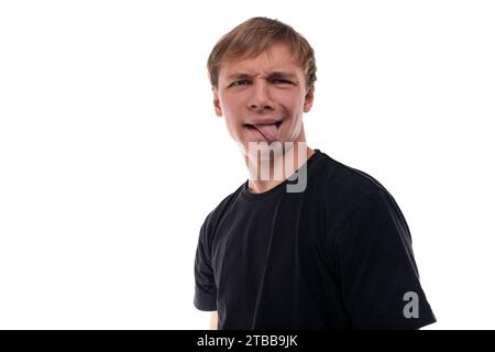 Cute teenage guy with blond hair dressed in a black T-shirt makes a face Stock Photo