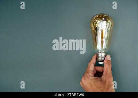 Hand holding yellow light bulb on gray background. Economical energy saving light bulb concept in man's hand. copy space Stock Photo