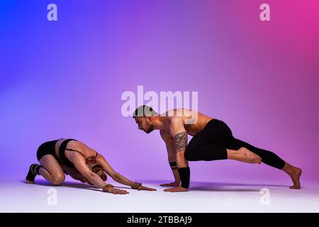Beautiful young acrobats or gymnasts with colorful face painting on pink blue gradient background. Professional ballet couple dancing, Emotional duet Stock Photo