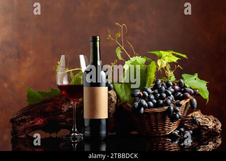 Glass and bottle of red wine with blue grapes and vine branches. On a bottle old empty label. Copy space. Stock Photo