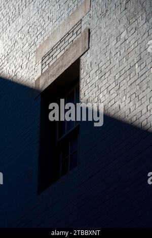 An old brick building and window all painted grey is covered by a diagonal line formed by shadow and light in Sydney, Australia Stock Photo