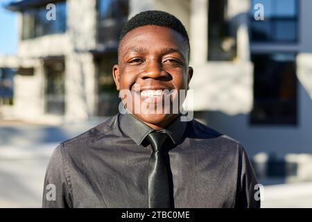 Portrait of young Black businessman smiling, wearing black shirt and tie Stock Photo