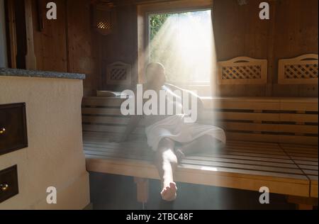 Man sitting in a sauna with light streaming through the window onto his relaxed figure. Stock Photo