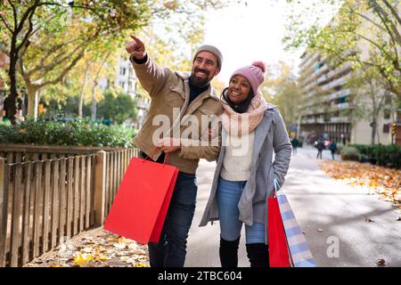 Multiracial couple walking in the city doing christmas shoppings together, pointing at things. Stock Photo