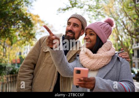 Young multiethnic couple using phone to look for a direction during winter holidays in the city. Stock Photo