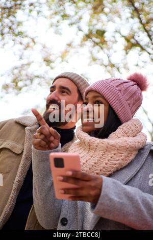 Young multiethnic couple using phone to look for a direction during winter holidays in the city. Stock Photo