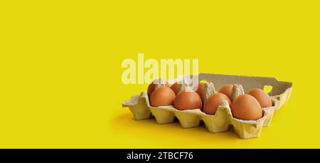 Rustic, organic brown chicken eggs in an open sustainable cardboard tray (box) on a bright, monochrome yellow background. Playful festive image Stock Photo