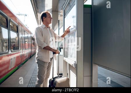 Passenger man searching train in timetable on train station in city. Stock Photo