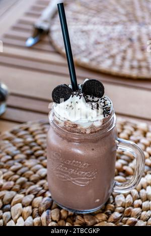 a freshly made chocolate milkshake topped with whipped cream and cookies at a restaurant. Stock Photo