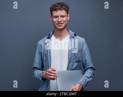 young man on a gray background holding a laptop Stock Photo