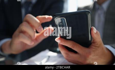 manager uses smartphone while sitting at table with colleague in office Stock Photo