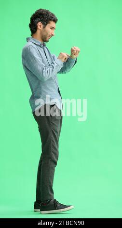 young man in full growth. isolated on green background looking at wristwatch Stock Photo
