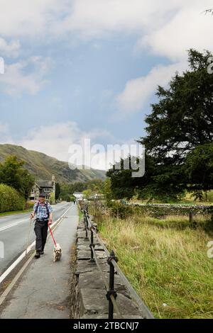 Male hiker with small dog on lead walking on a footpath at Patterdale, Lake District, Cumbria Stock Photo