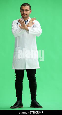 male doctor in a white coat on a green background shows a cancel sign Stock Photo