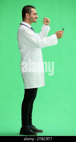 male doctor in a white coat on a green background looking at the phone Stock Photo