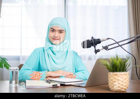 Muslim woman wearing hijab and headphones listening to audiobooks and podcasts at home, satisfied and successful woman. Stock Photo
