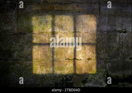 Soft light shining through a window frame on to an old stone wall with moss Stock Photo