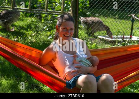 Young mother with newborn child in the hammock in the garden. Mecklenburg-Western Pomerania, Germany Stock Photo