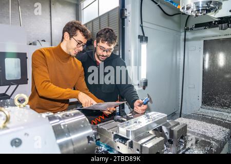 Two male engineers examining pieces next to a milling machine in a cnc modern factory Stock Photo
