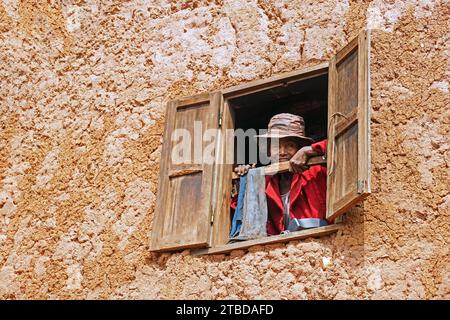 Elderly Malagasy woman looking from window in two stories mud house in the Ambositra District, Amoron'i Mania Region, Central Madagascar, Africa Stock Photo