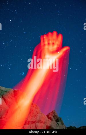 Arms reaching and waving in red light taken with a starry desert landscape in the background. Stock Photo